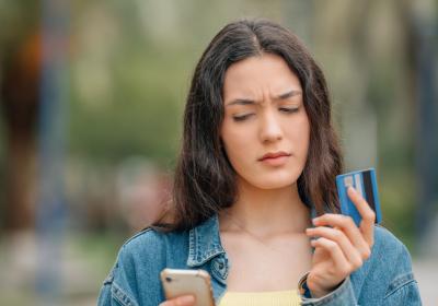 Vrouw met bankpas in hand kijkt verontrust naar telefoon